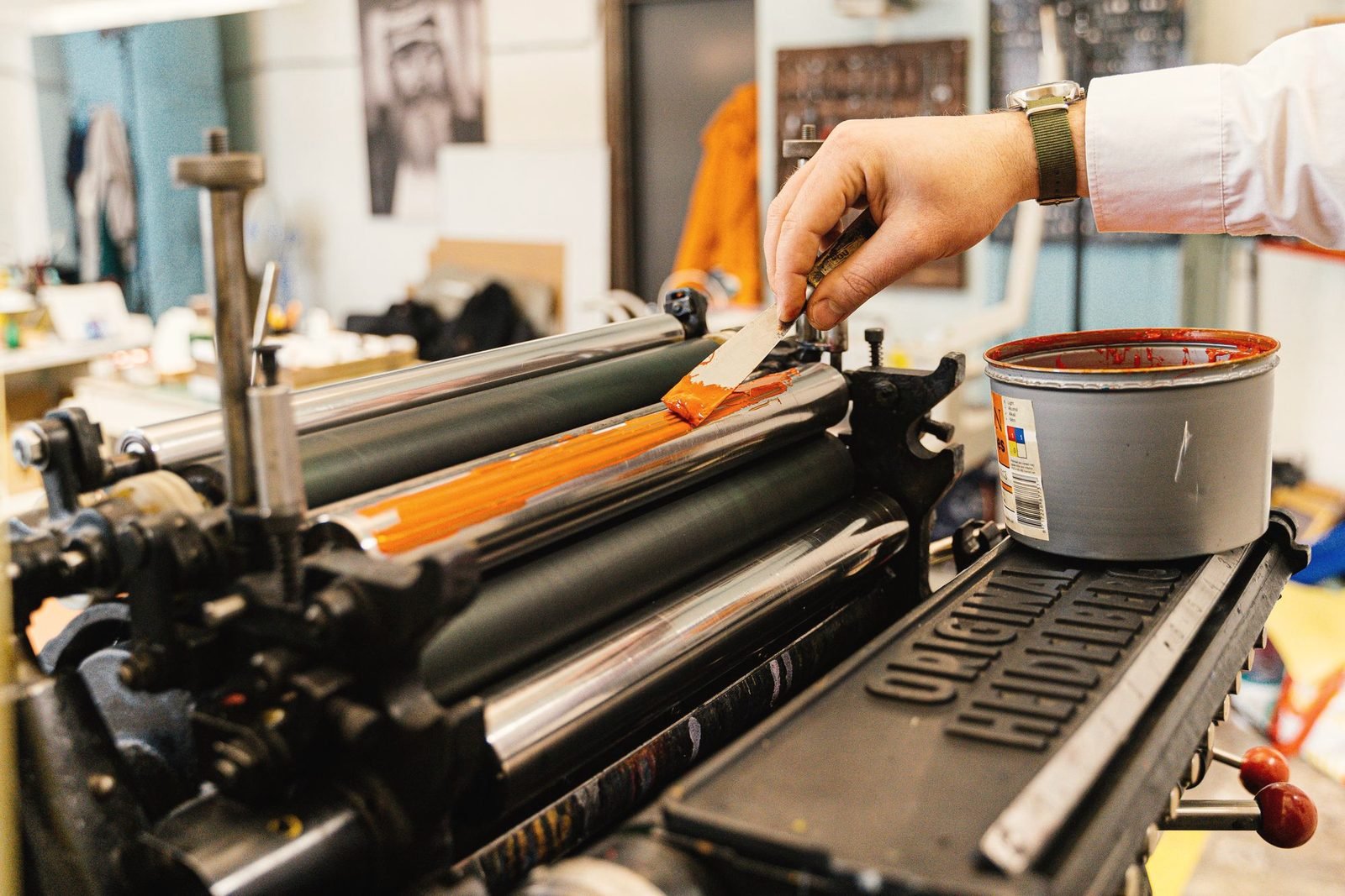 A hand spreading orange ink onto the rollers of a press